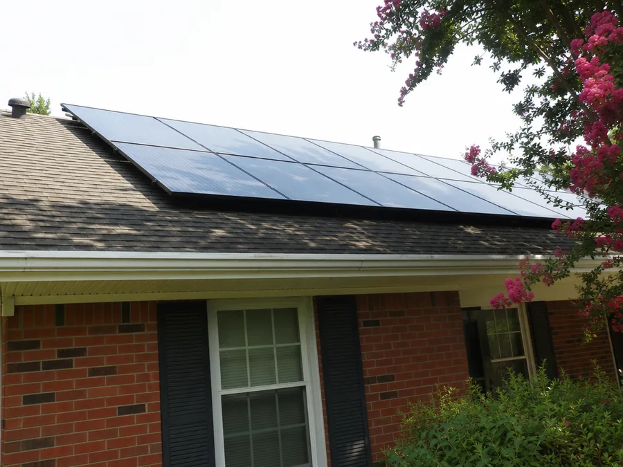Solar modules on the low pitch shingle roof of a single storey brick house, seen obliquely from the front yard